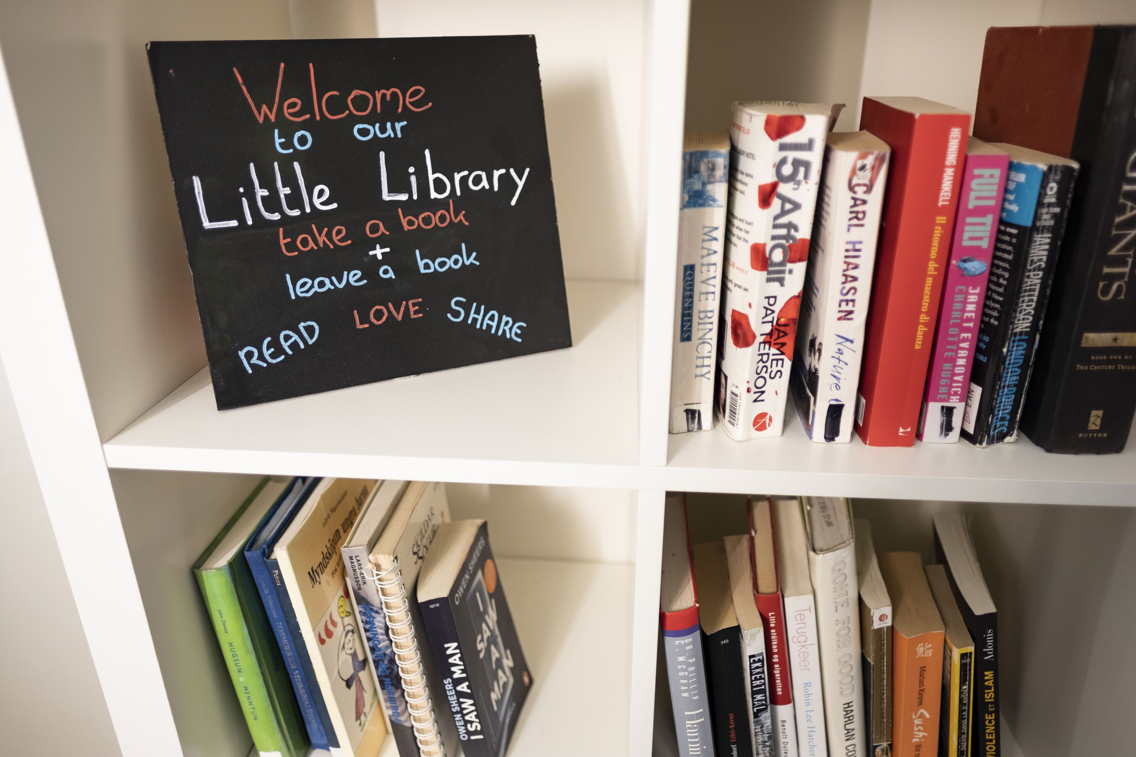A bookshelf with a sign that reads "Welcome to our Little Library" and encourages reading, loving, and sharing books.