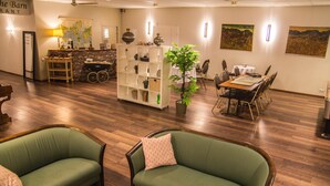 A hotel lobby with a wooden floor, two green sofas, a white shelving unit, a dining table with chairs, and a potted plant. - Hotel Fljotshlid (Rangárþing eystra)