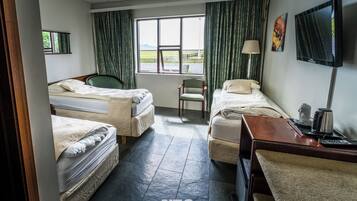A hotel room with two beds, a desk, a chair, a TV, and a window with a view of the outdoors.