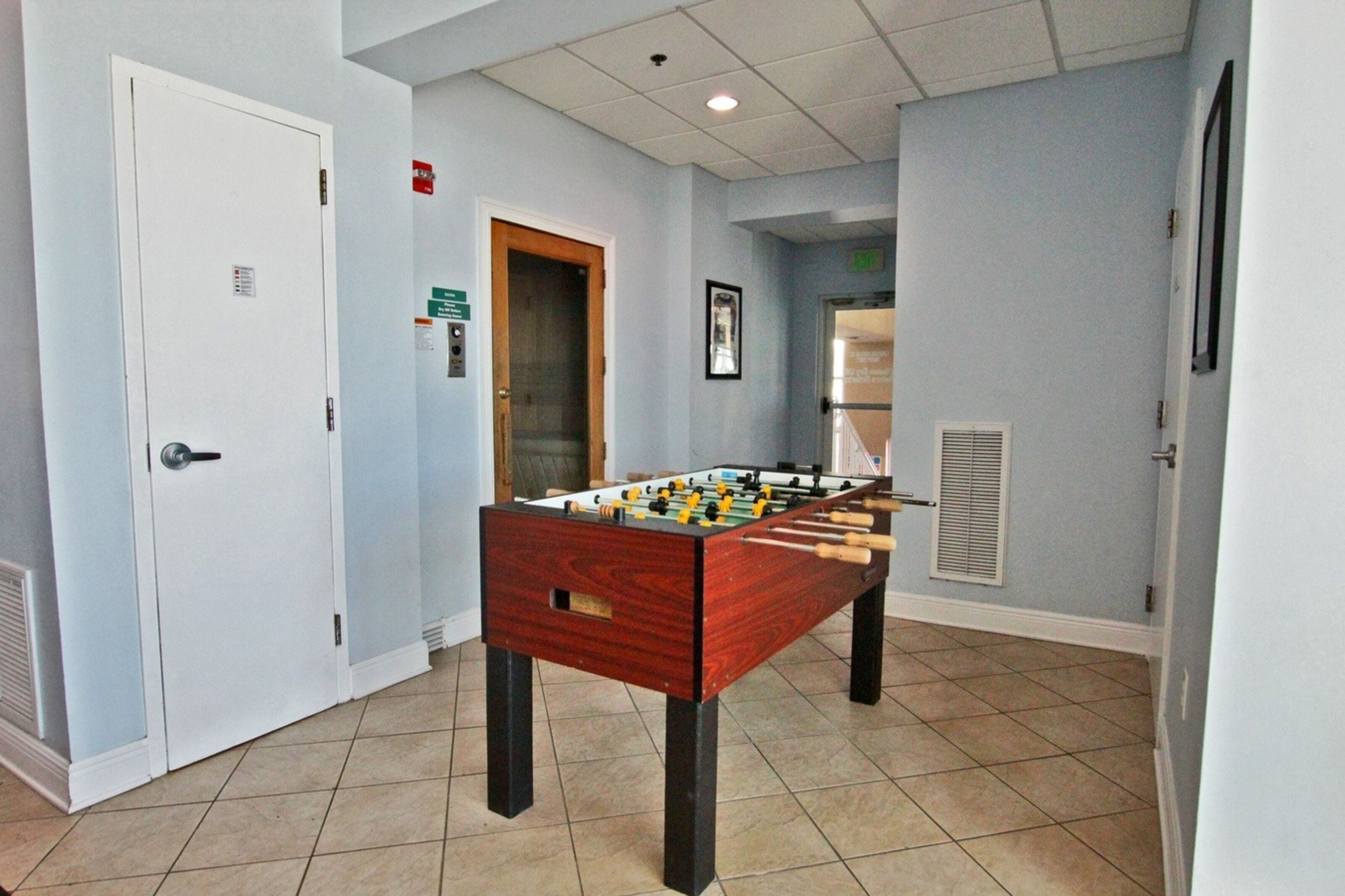 Une pièce avec une table de baby-foot, une porte et une grille d’aération au mur.