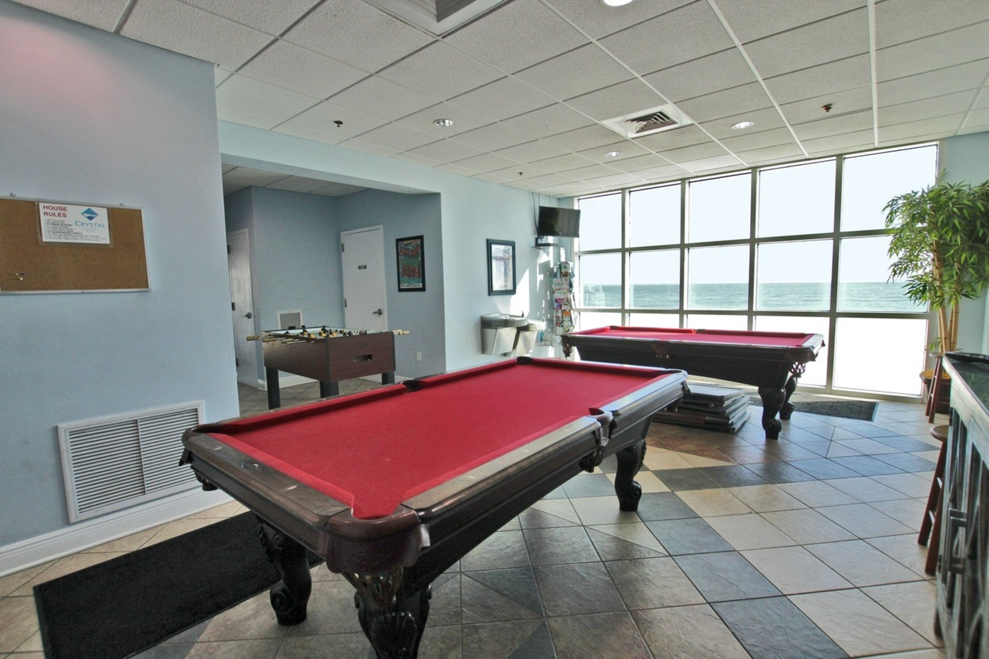 Une table de billard recouverte d’un feutre rouge, une deuxième table en arrière-plan et une grande fenêtre donnant sur l’océan.
