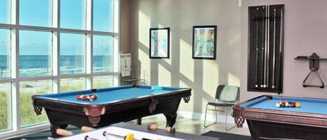 A room with two foosball tables, a pool table, and a window overlooking the ocean.