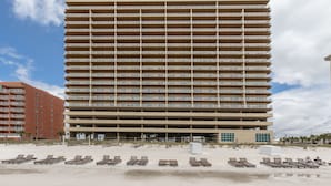 Een hoog hotel met meerdere balkons, een ligging aan het strand en een zandstrand met ligbedden.