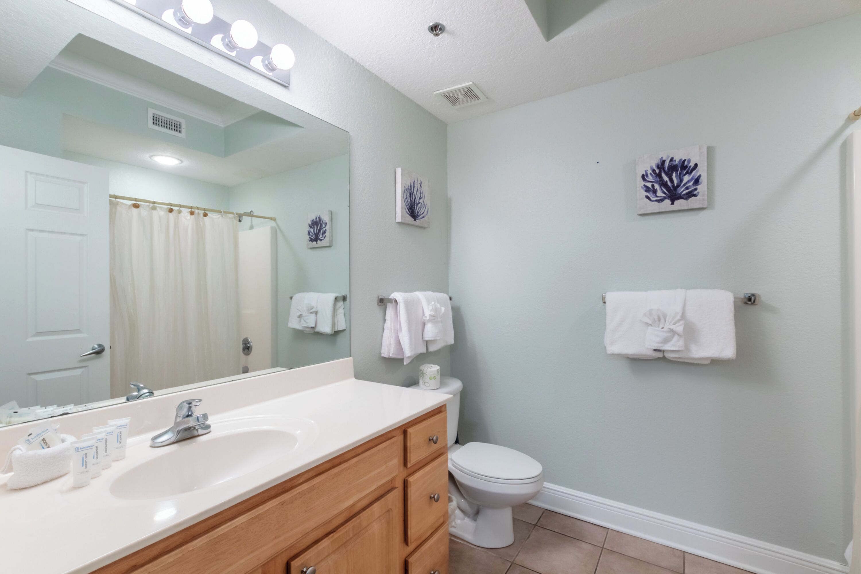 Une salle de bain avec un lavabo blanc, un meuble-lavabo en bois, un grand miroir, des toilettes blanches et deux porte-serviettes fixés au mur.