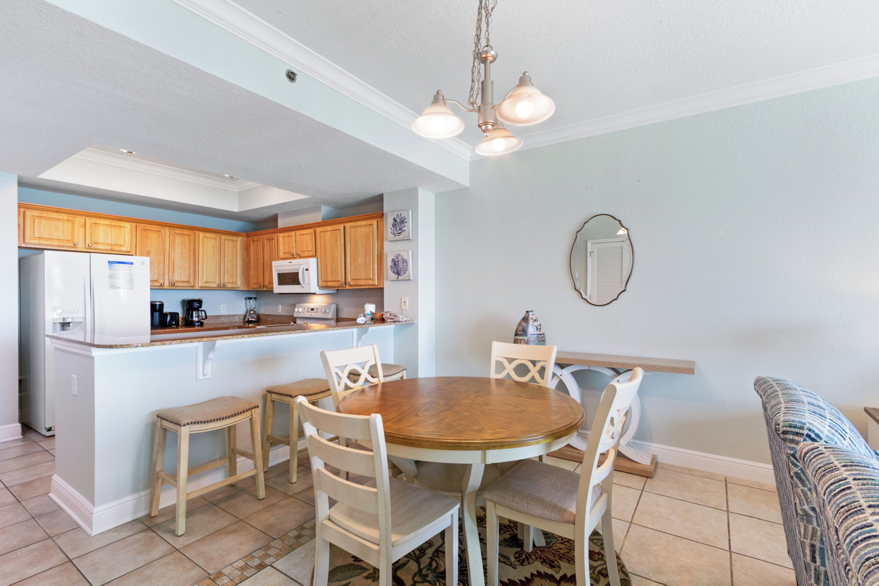 A kitchen with wooden cabinets, a white refrigerator, a microwave, and a dining table with chairs.