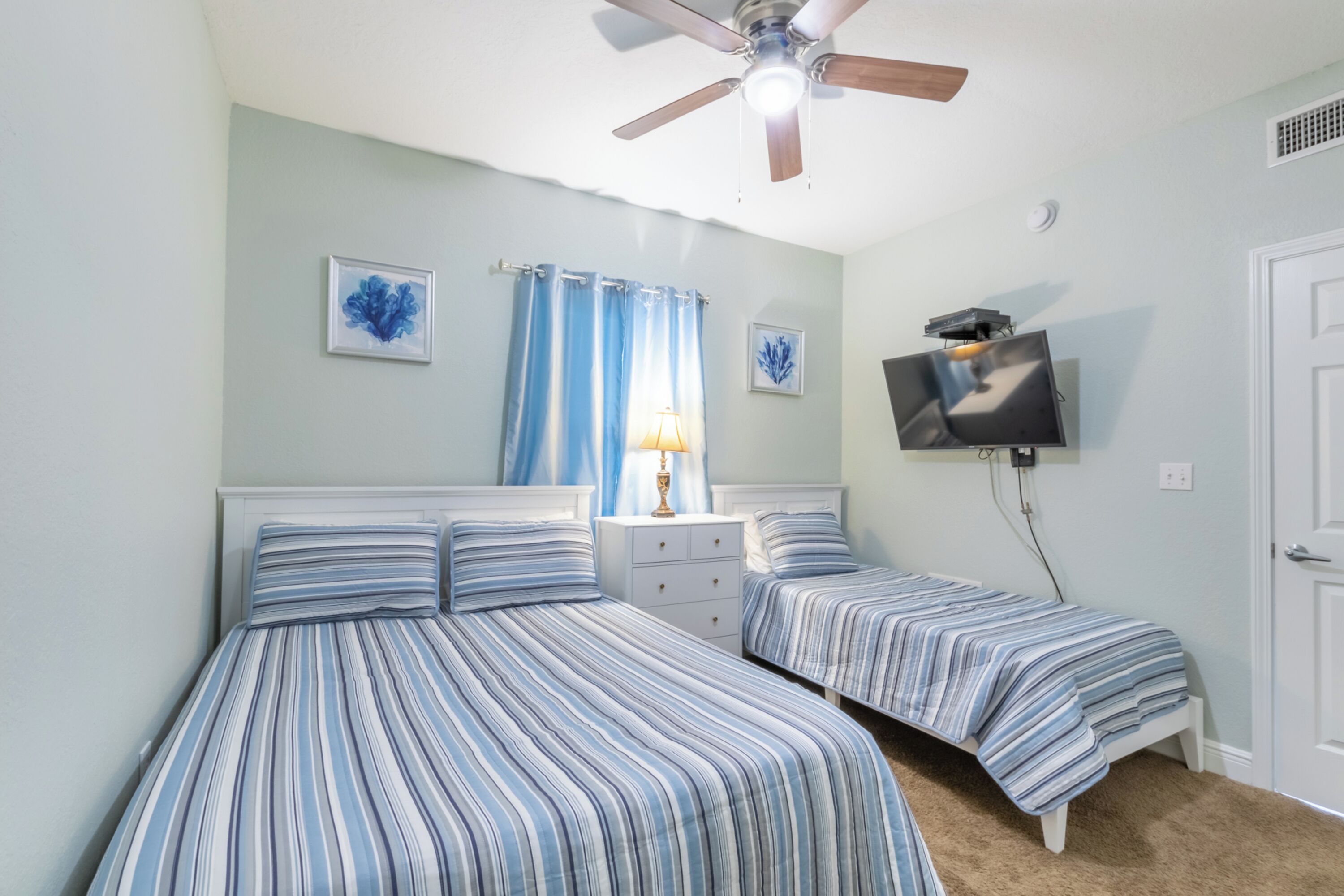 A bedroom with two beds, a ceiling fan, a TV, and a nightstand with a lamp.