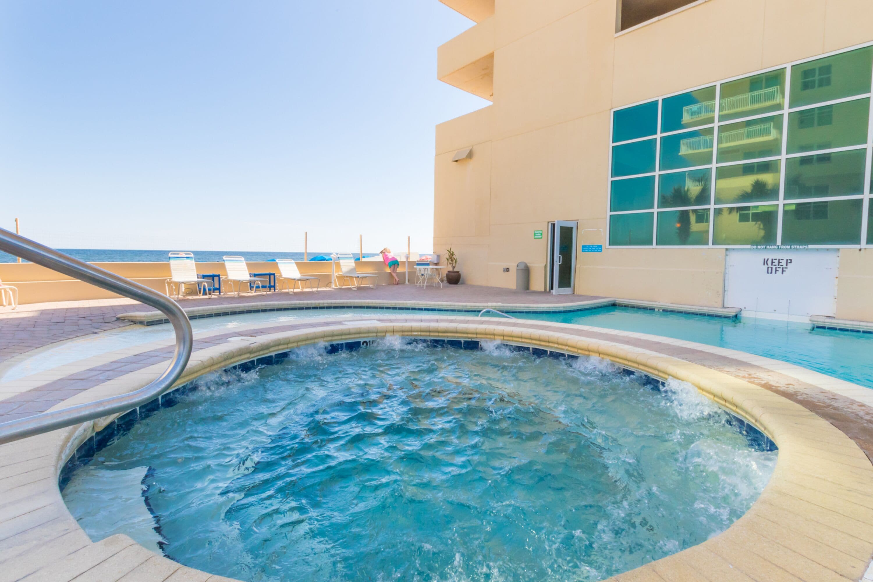 A hot tub area with a pool, lounge chairs, and a building with large windows.
