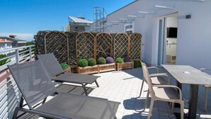 A rooftop terrace with metal chairs and tables, a wooden fence, and a small garden with spherical plants. - Hotel Manù (Rimini)