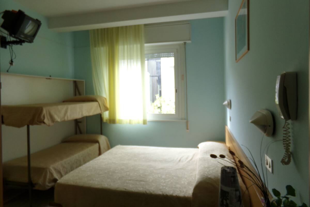 A room with bunk beds, a window with curtains, a telephone, and a television mounted on the wall.