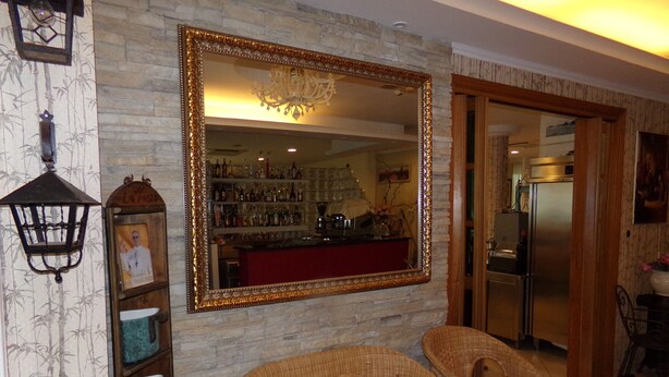 A room with wicker chairs, a large mirror, and a bar area visible through the mirror. - Hotel Manù (Rimini)