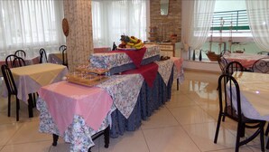 A dining area with tables set for a meal, a fruit display, and a view of the sea through large windows. - Hotel Manù (Rimini)