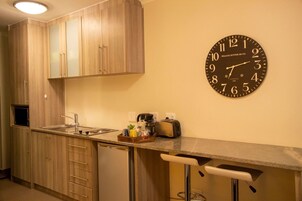Una cocina compacta con armarios de madera, un lavamanos, un tostador y un reloj en la pared.