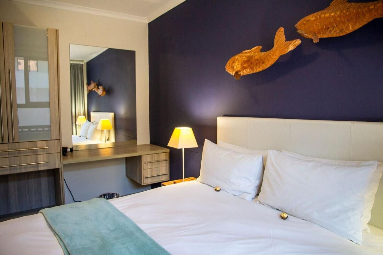 Een hotelkamer met een bed, een bureau, een spiegel en een visbeeld aan de muur.