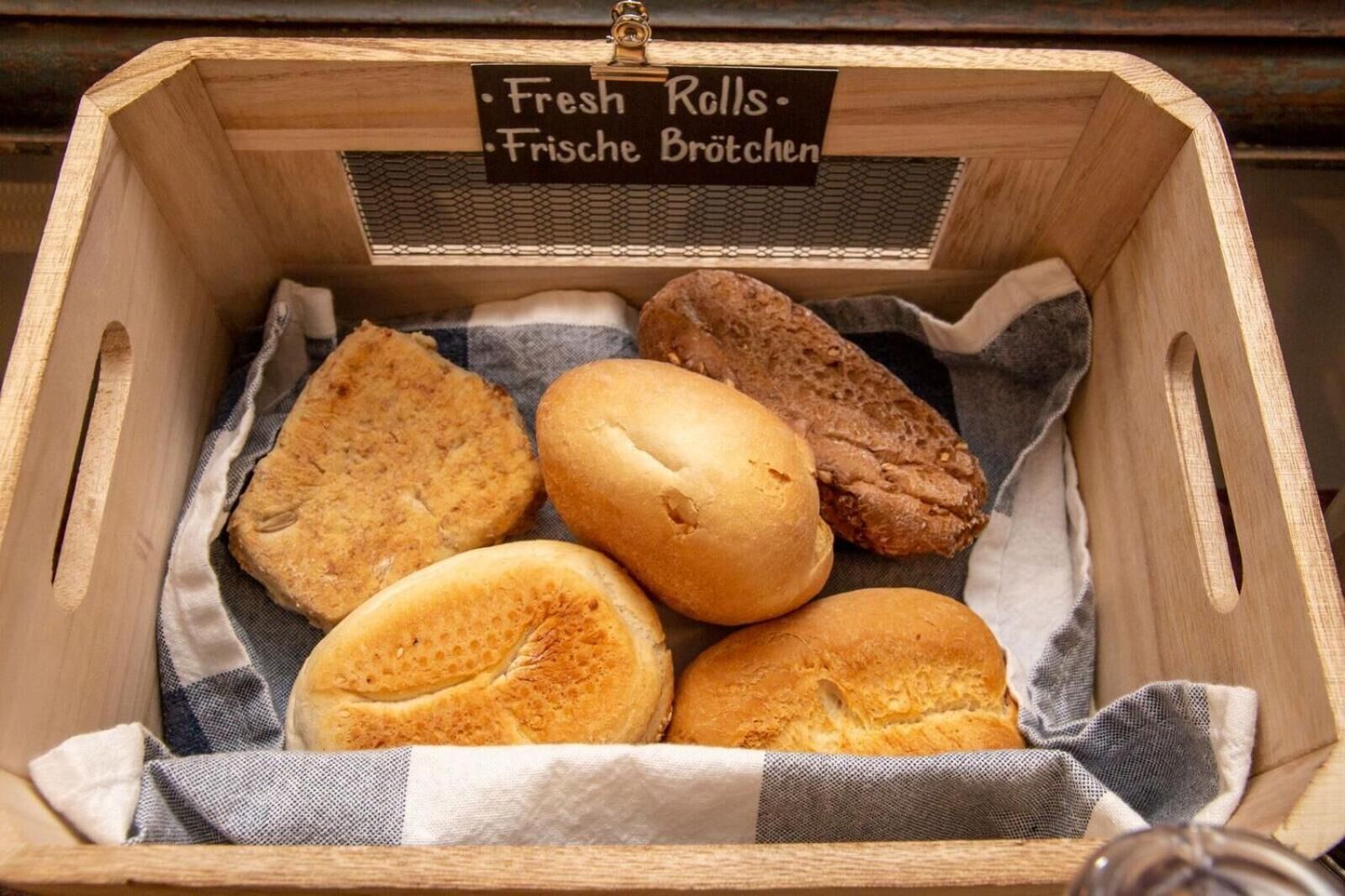 A wooden box containing various types of bread, labeled "Fresh Rolls - Frische Brötchen."