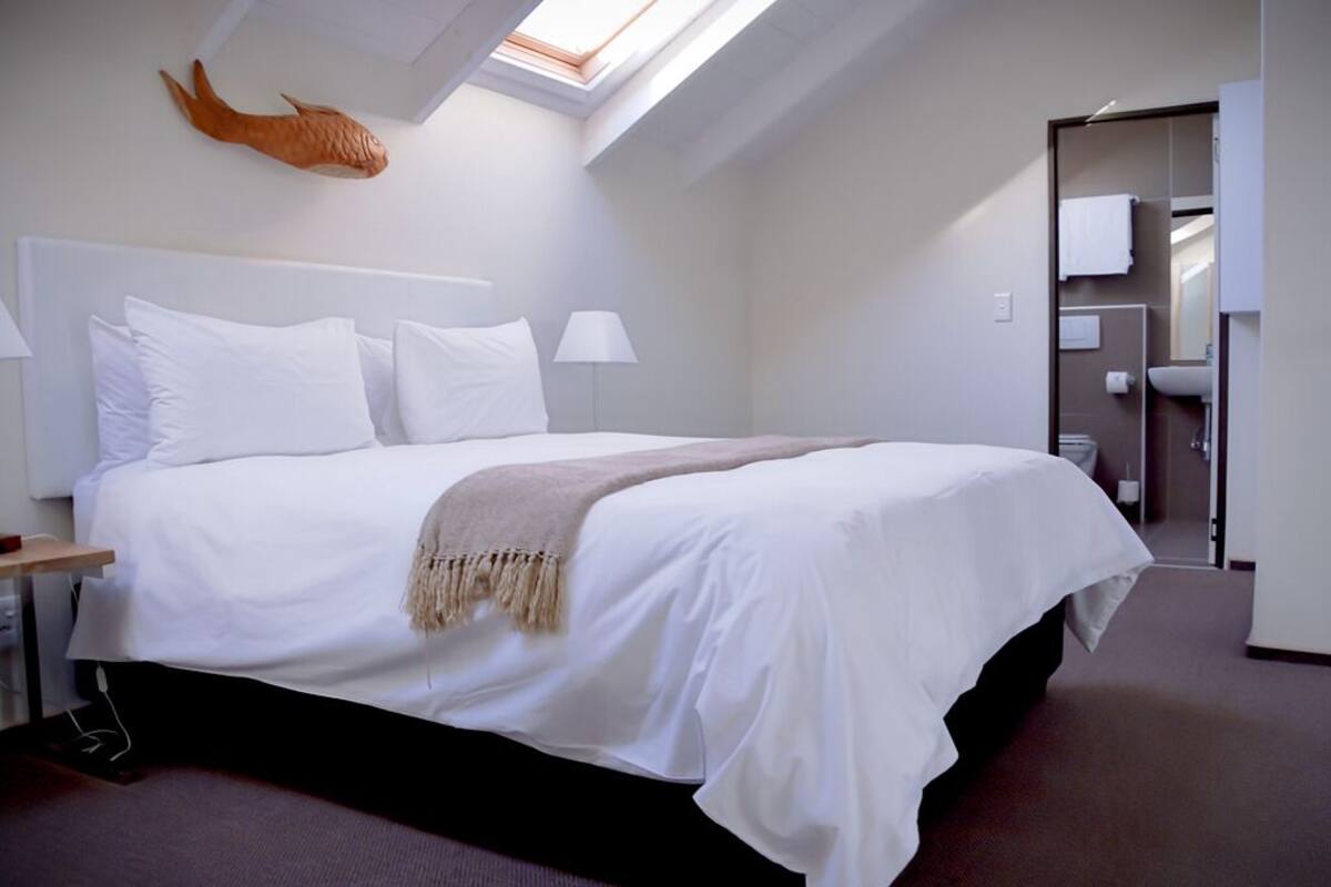 A hotel room with a large bed, a skylight, a fish decoration on the wall, and a bathroom visible through an open door.