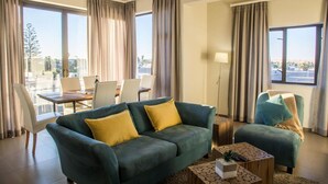 A modern hotel room with a green sofa, yellow cushions, a wooden coffee table, and a view of the city through large windows. - Desert Sands Boutique B&B - Self-Catering (Swakopmund)