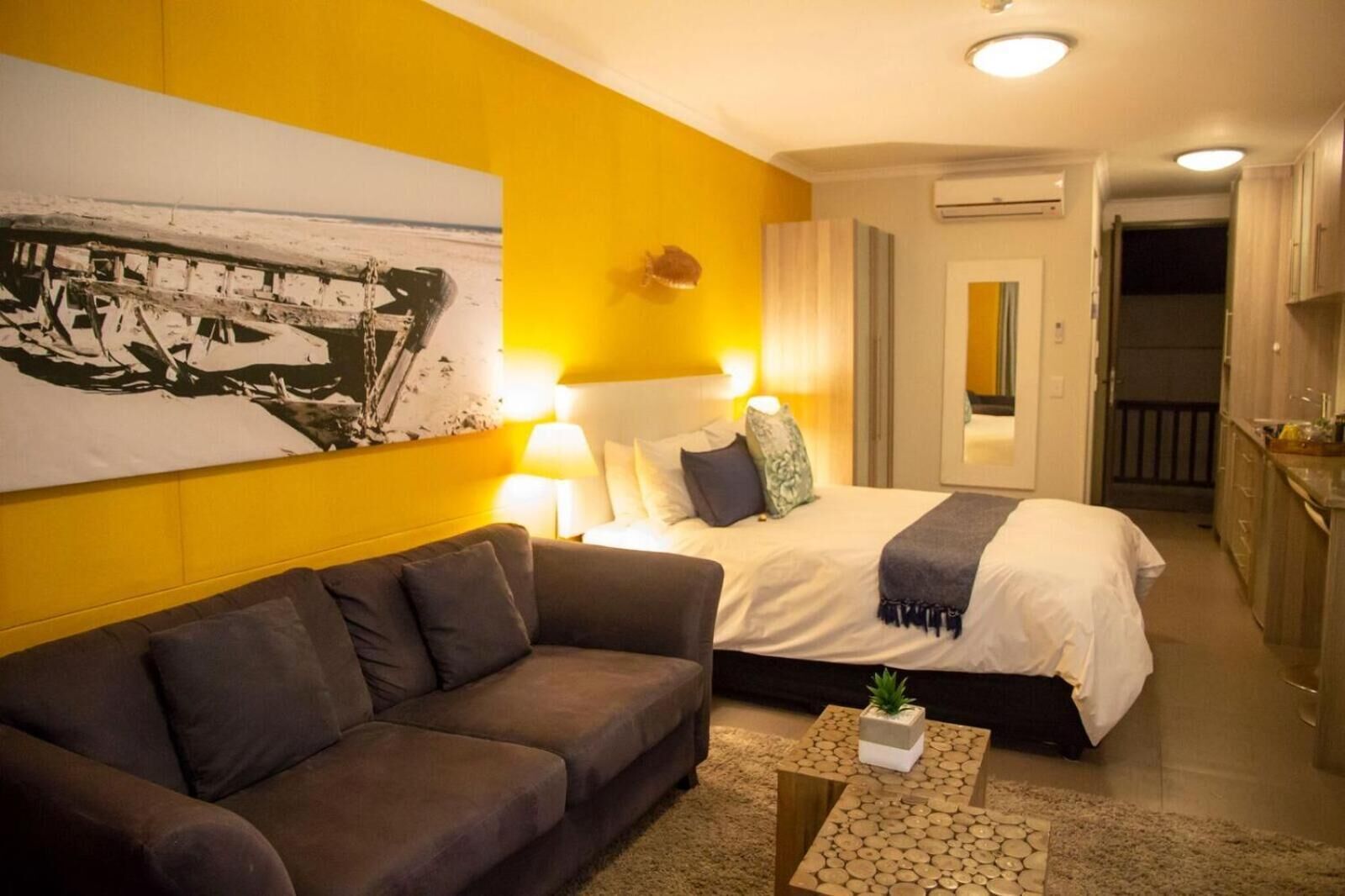 Una habitación de hotel con una cama, un sofá, una mesita con una planta y un cuadro en la pared.