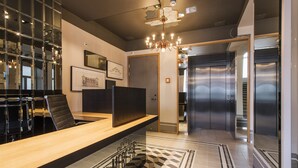 A modern reception area with a long wooden counter, black leather chairs, a chandelier, and a geometric patterned floor. - Lighthouse Apartments Tallinn (Tallinn)