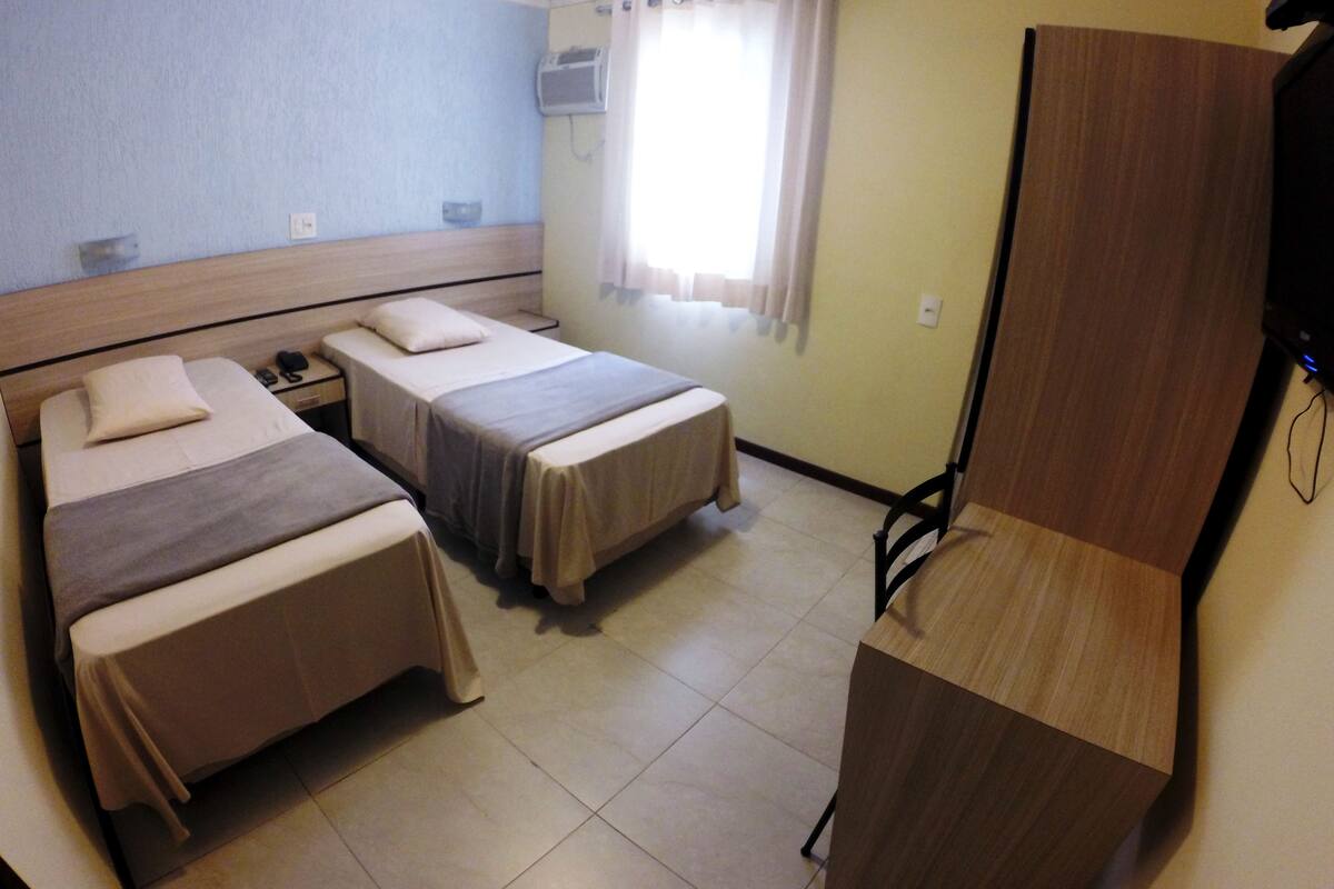 A hotel room with two beds, a wooden desk, a TV, and a window with curtains.