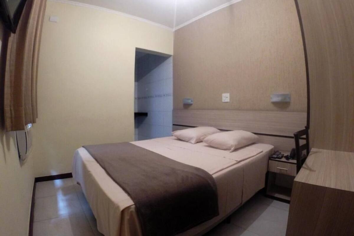 A hotel room with a bed, bedside table, and a mirror.