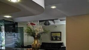 A modern lobby with a curved reception desk, a vase with flowers, a black sofa, and a painting on the wall. - Hotel Brigadeiro (São Paulo)