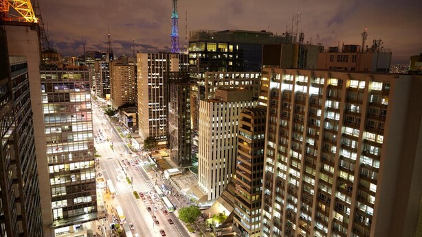 A nighttime cityscape with high-rise buildings, a prominent tower with illuminated spires, and a busy street below. - Hotel Brigadeiro (São Paulo)