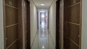 A long, narrow hotel corridor with wooden doors on either side, numbered signs above each door, and a shiny tiled floor. - Hotel Brigadeiro (São Paulo)