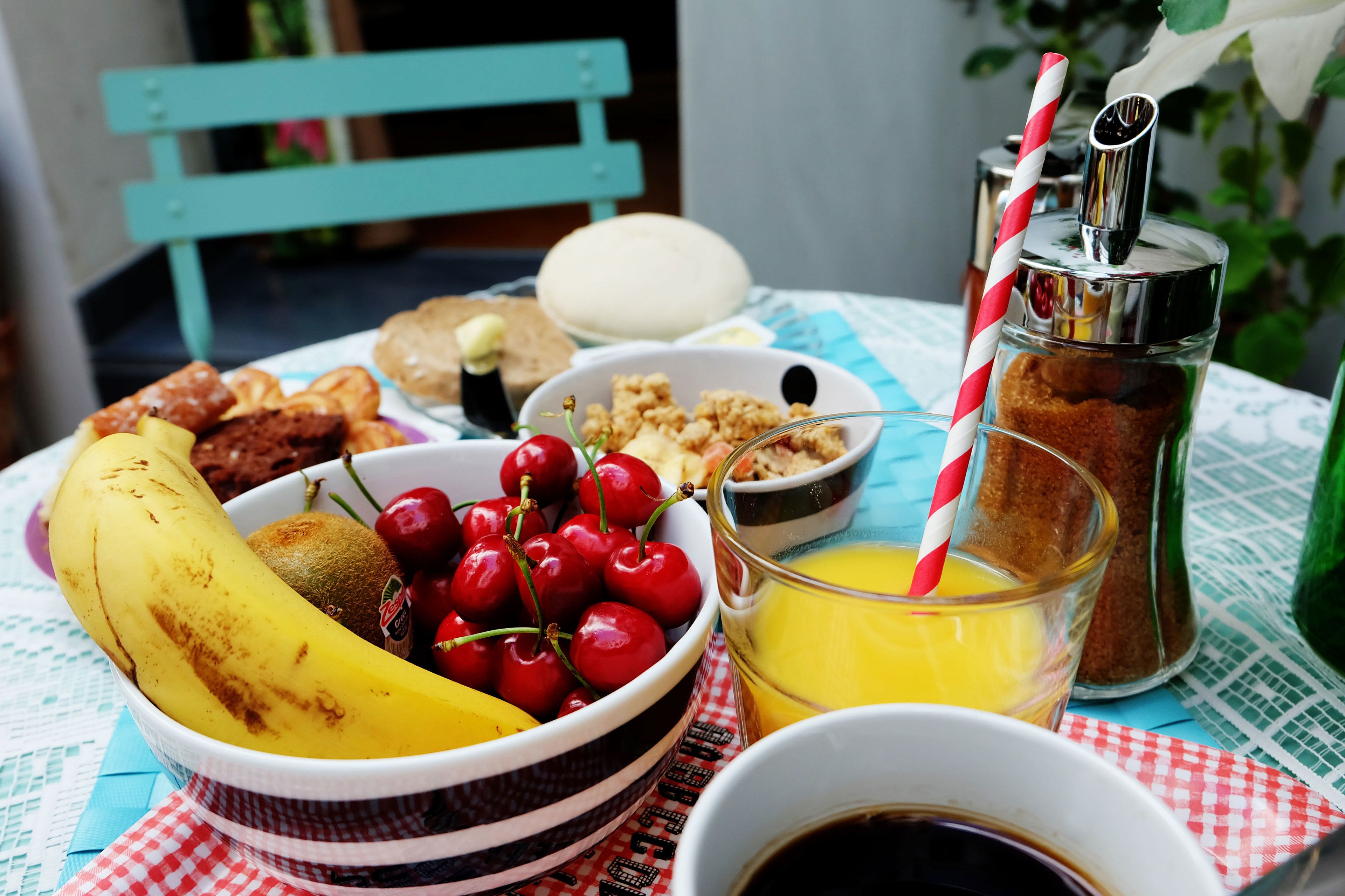 Une table où sont présentés divers aliments pour le petit-déjeuner, notamment un saladier de fruits, un verre de jus d’orange et une tasse de café.