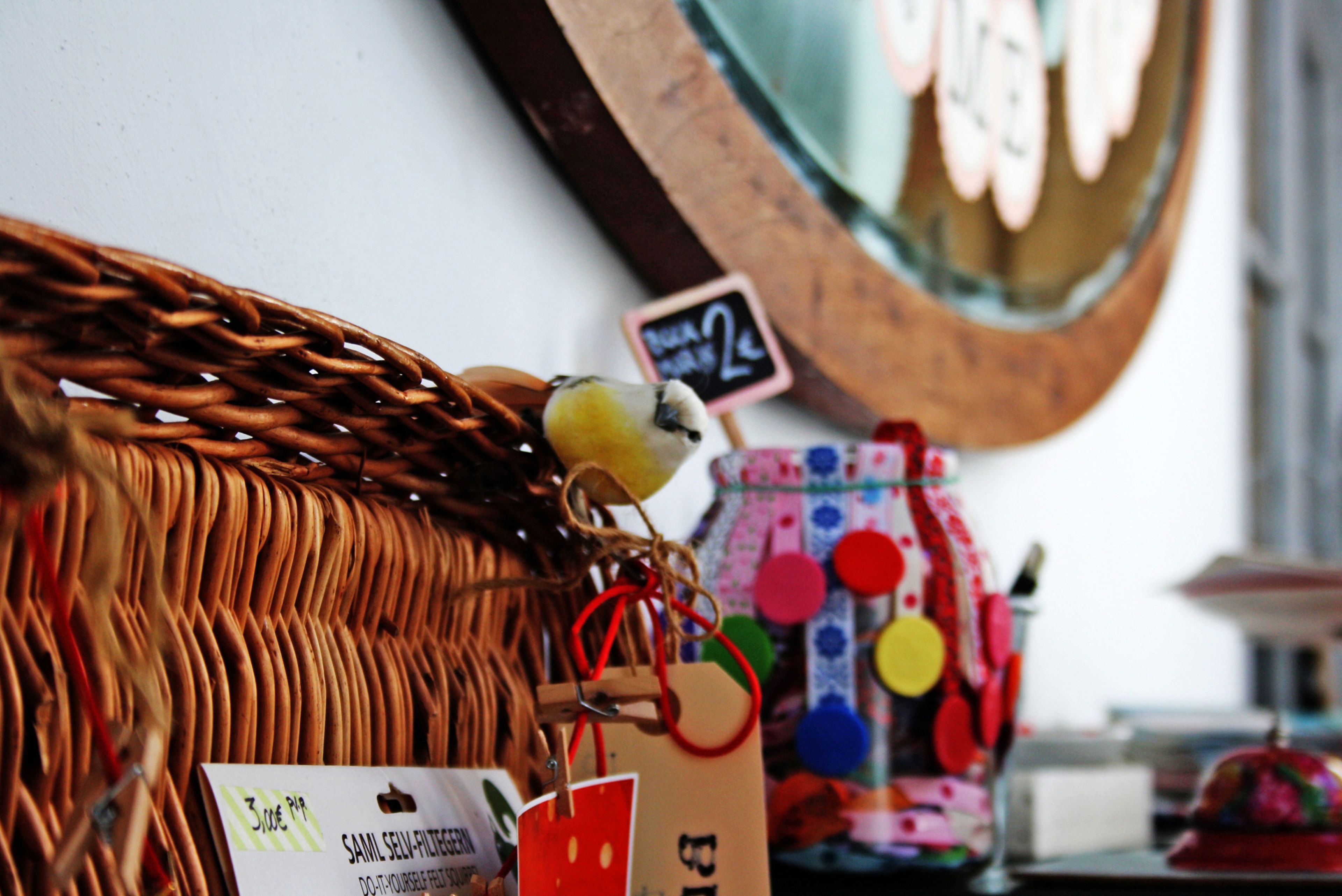Una cesta de mimbre con un pájaro, un florero colorido y un cartel con texto.
