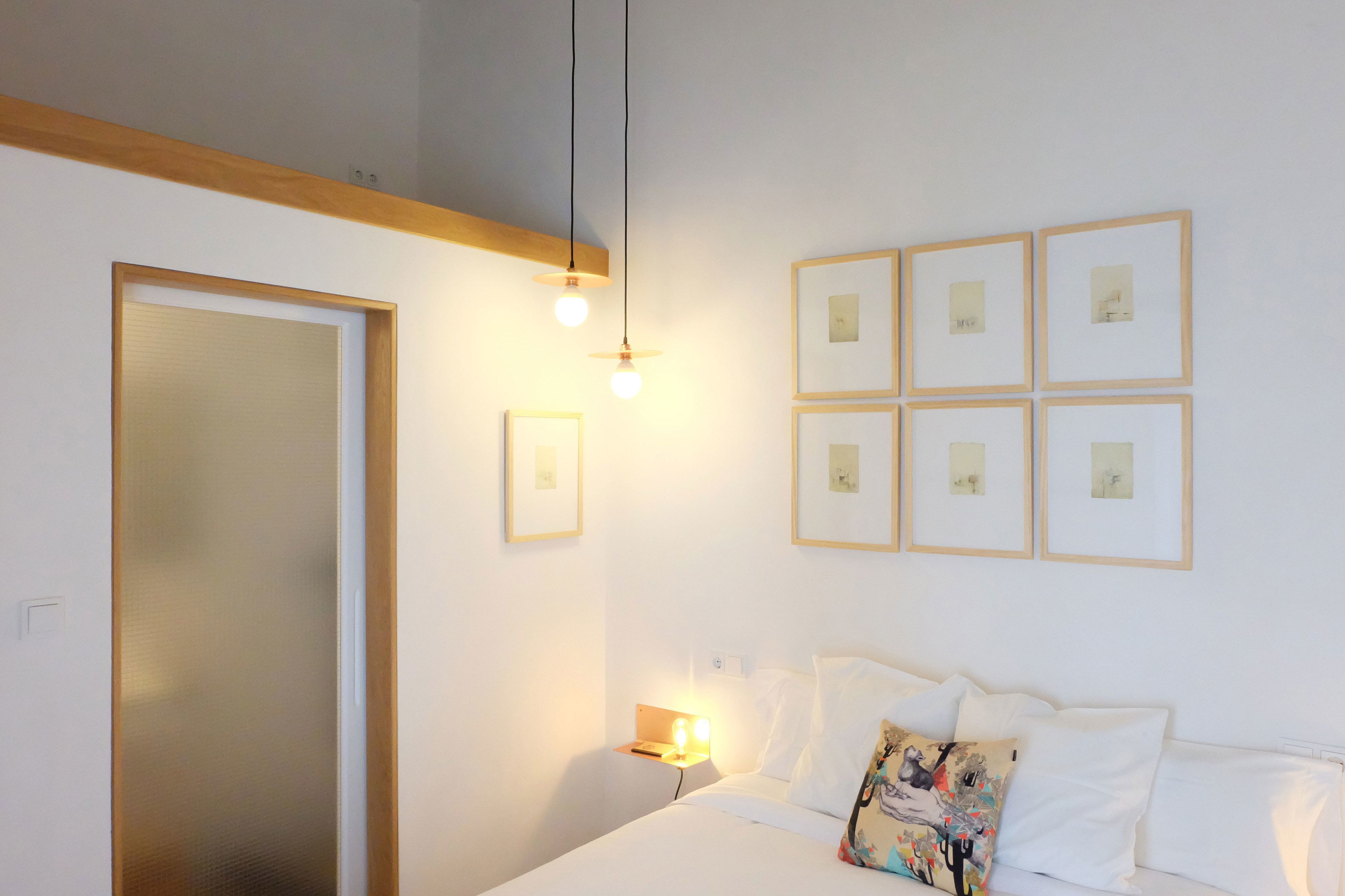 Un dormitorio con cama, mesita de noche, luces empotradas en la pared y cuadros enmarcados.