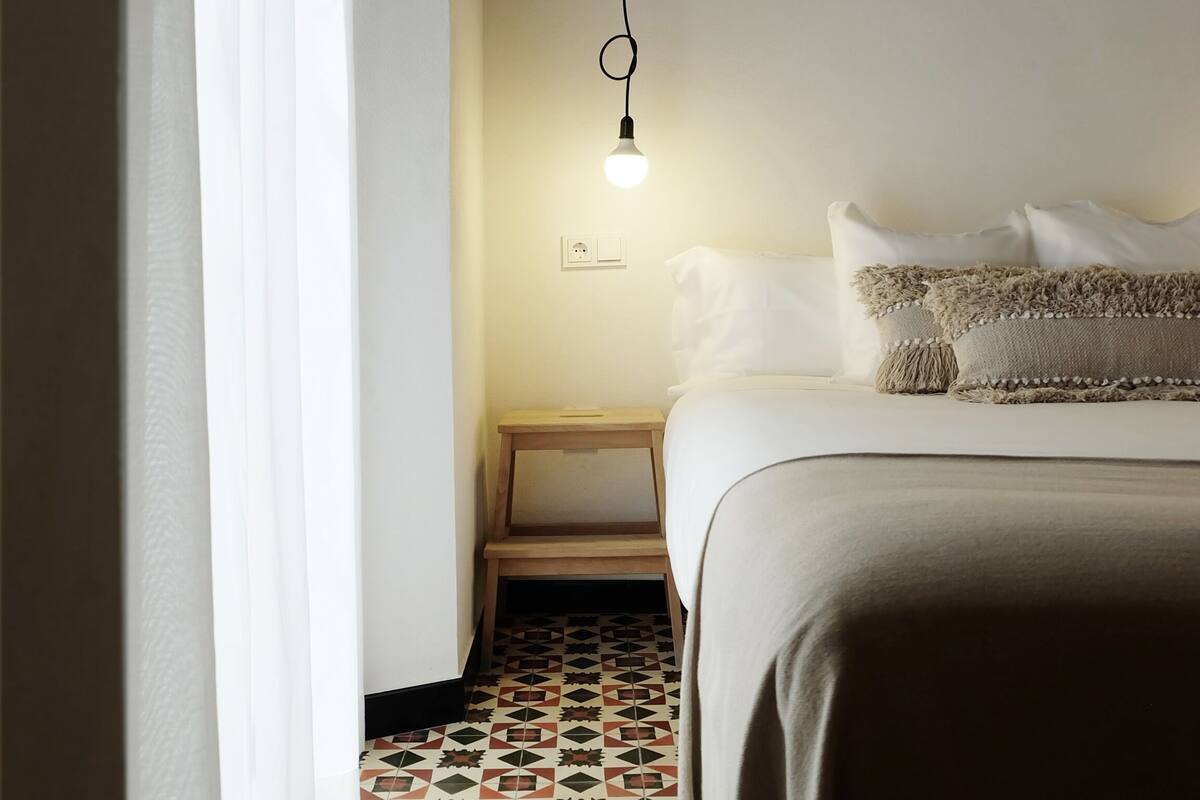 A bedroom with a bed, a nightstand, a hanging light, and patterned floor tiles.
