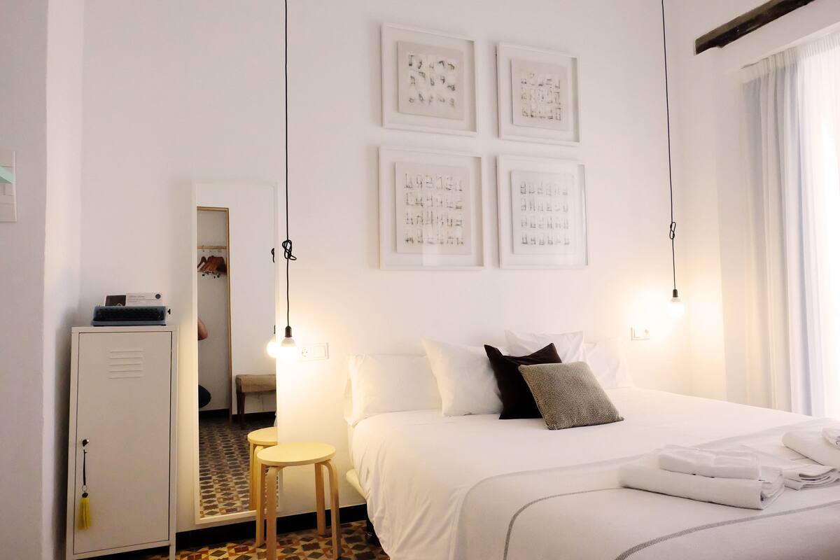 A hotel room with a bed, bedside tables, a wardrobe, and framed pictures on the wall.