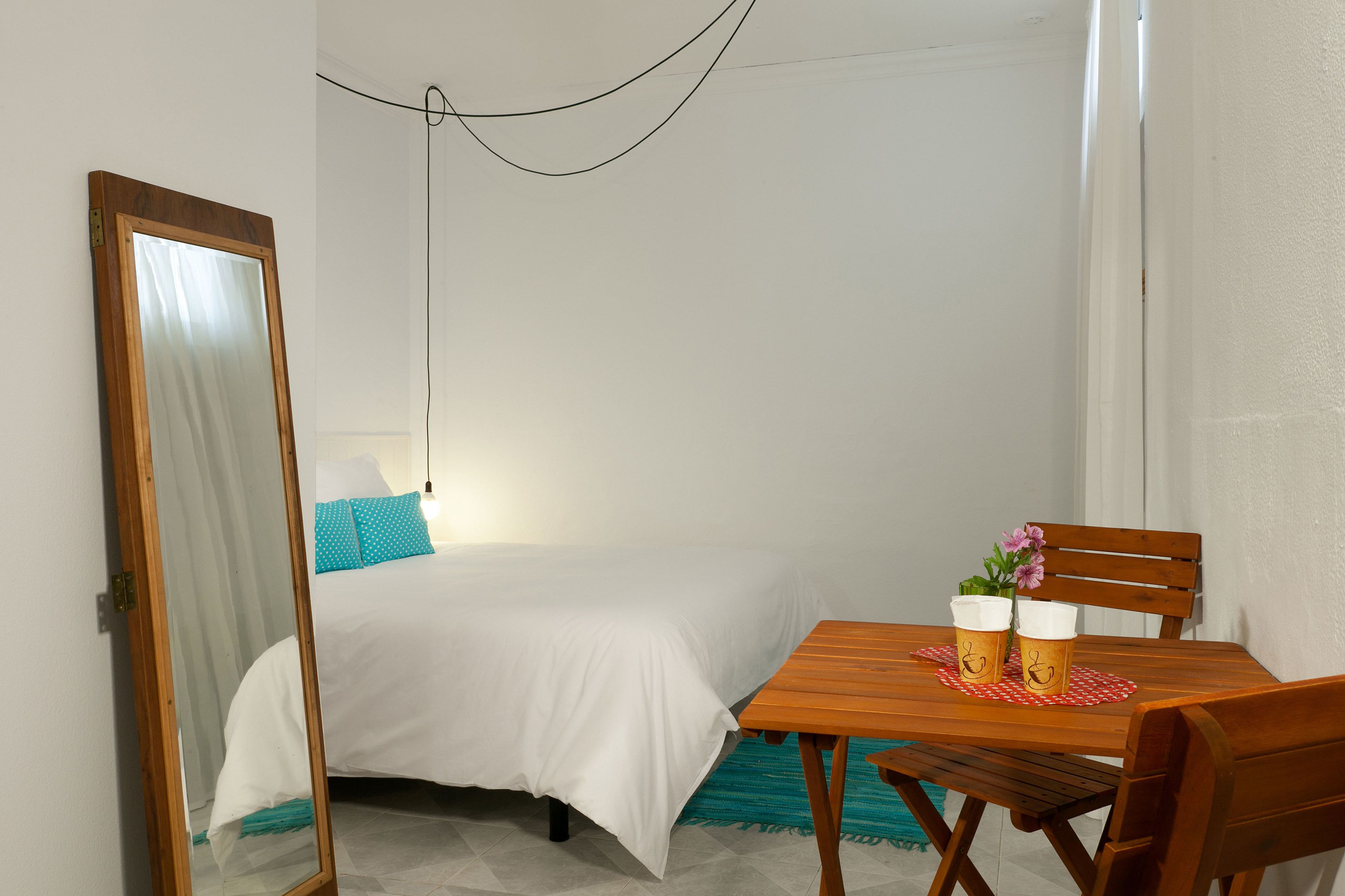 A bedroom with a bed, a wooden table with two cups, and a mirror.