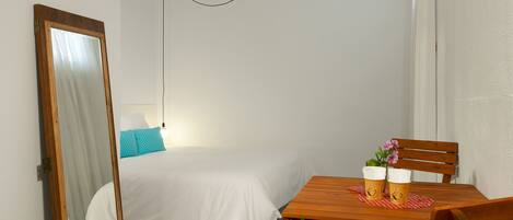 A bedroom with a bed, a wooden table with two cups, and a mirror.
