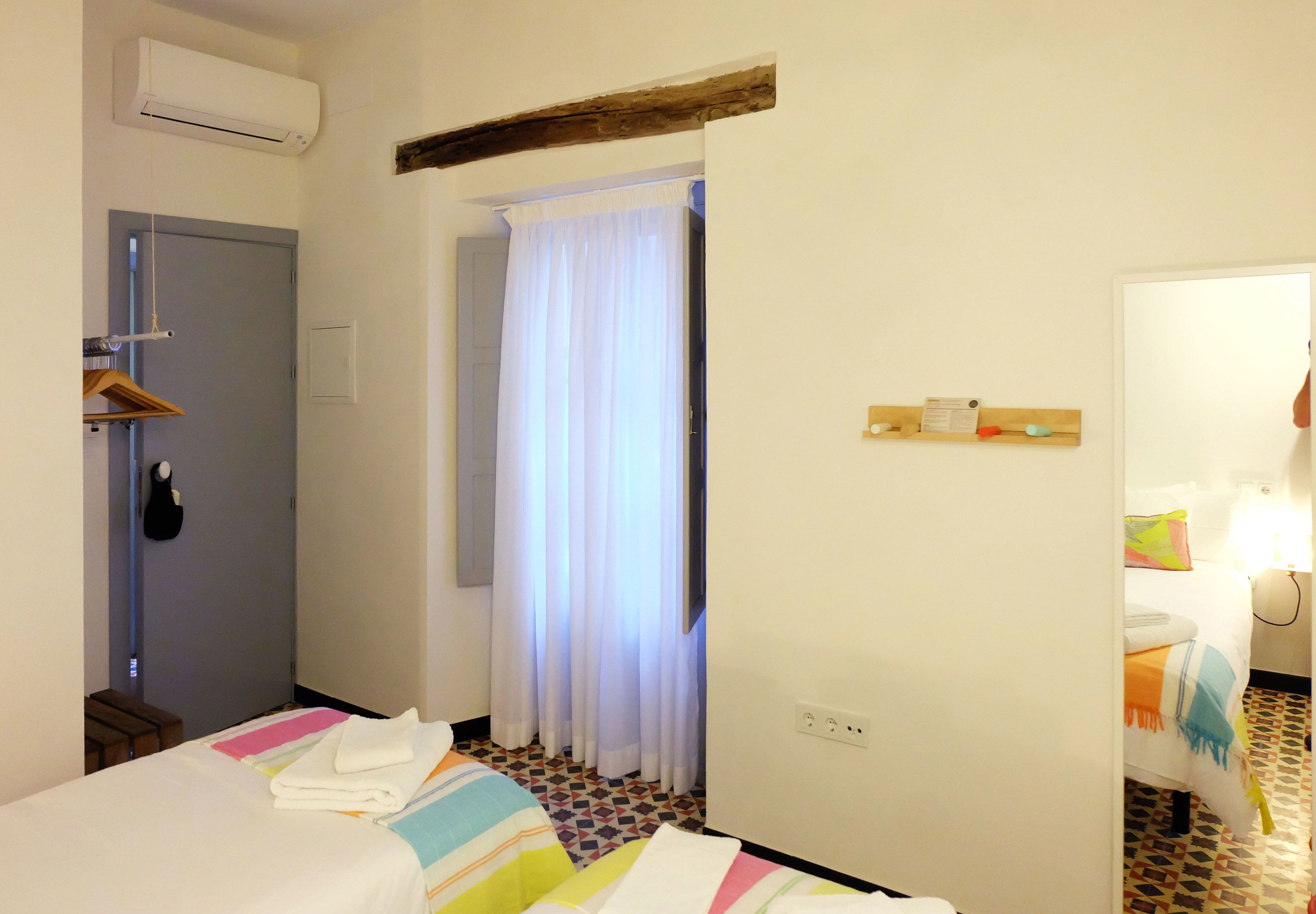 A hotel room with a bed, a shower area, a towel rack, and a small wooden shelf with toiletries.