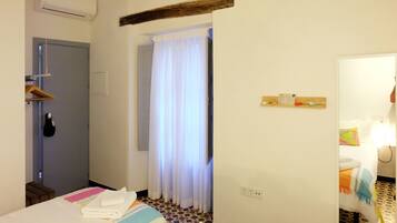 A hotel room with a bed, a shower area, a towel rack, and a small wooden shelf with toiletries.