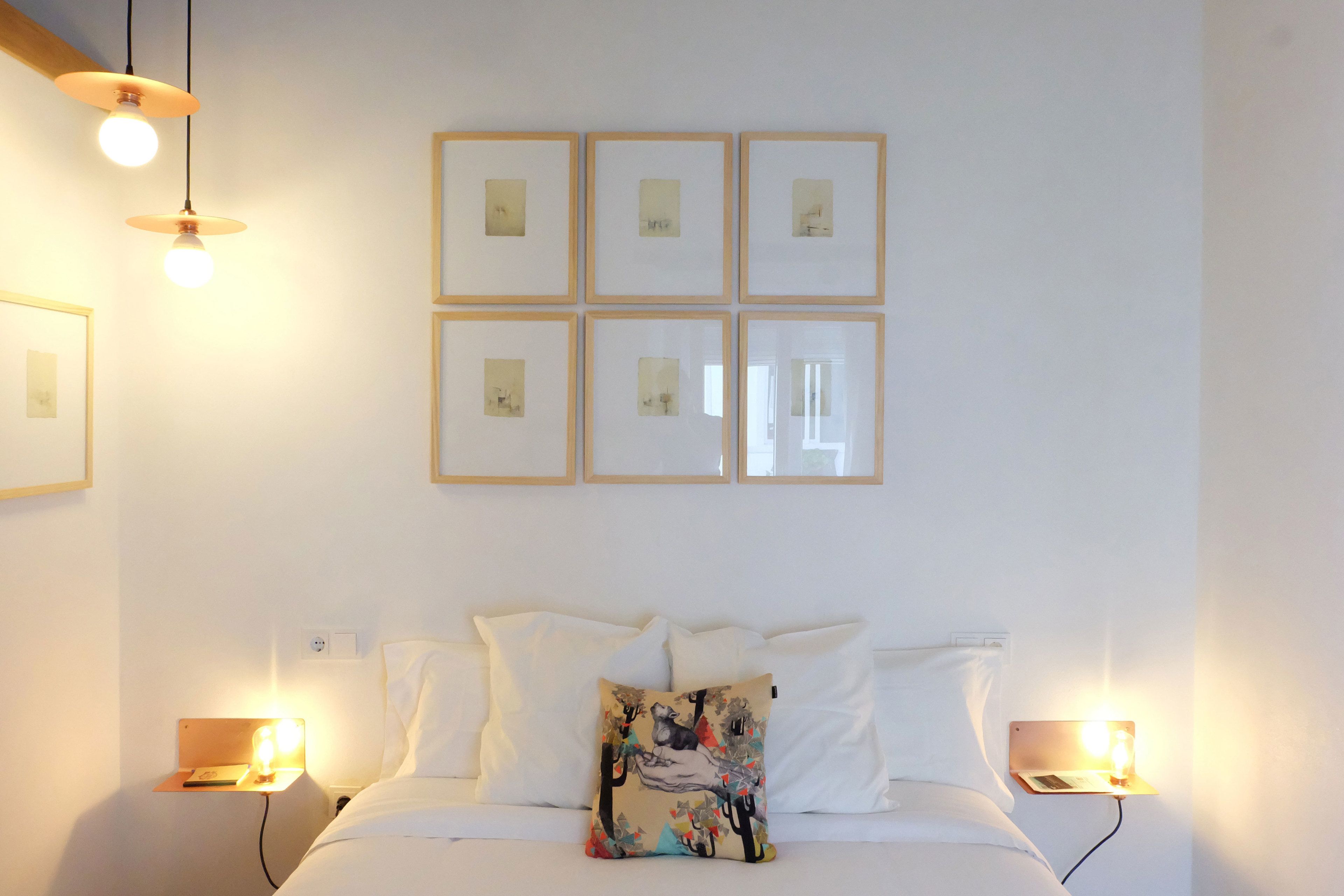 A neatly arranged hotel room with a bed, white bedding, a colorful pillow, and framed pictures on the wall.