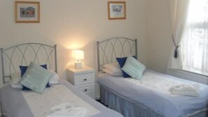 A bedroom with two single beds, a nightstand with a lamp, and a window with curtains. - Fourways Guest House (Thirsk)