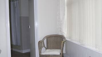 A room with a patterned carpet, a wicker chair, a wooden table, and a window with sheer curtains.