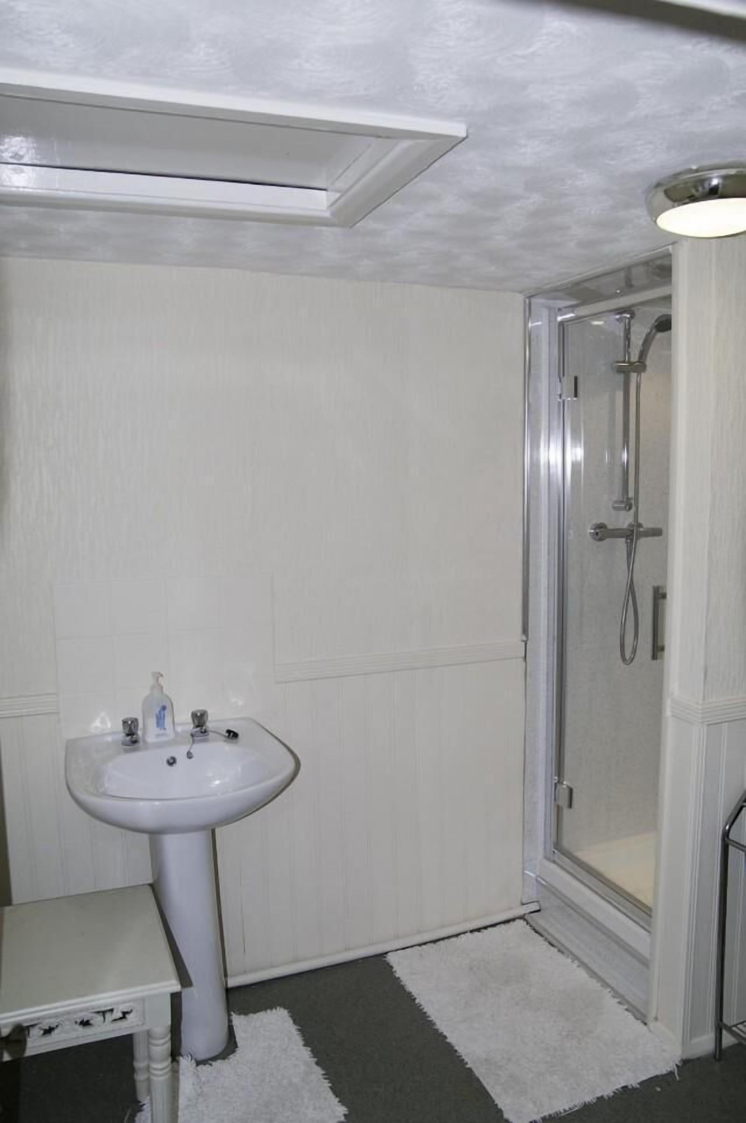A bathroom with a white pedestal sink, a glass shower enclosure, and a white rug on the floor.