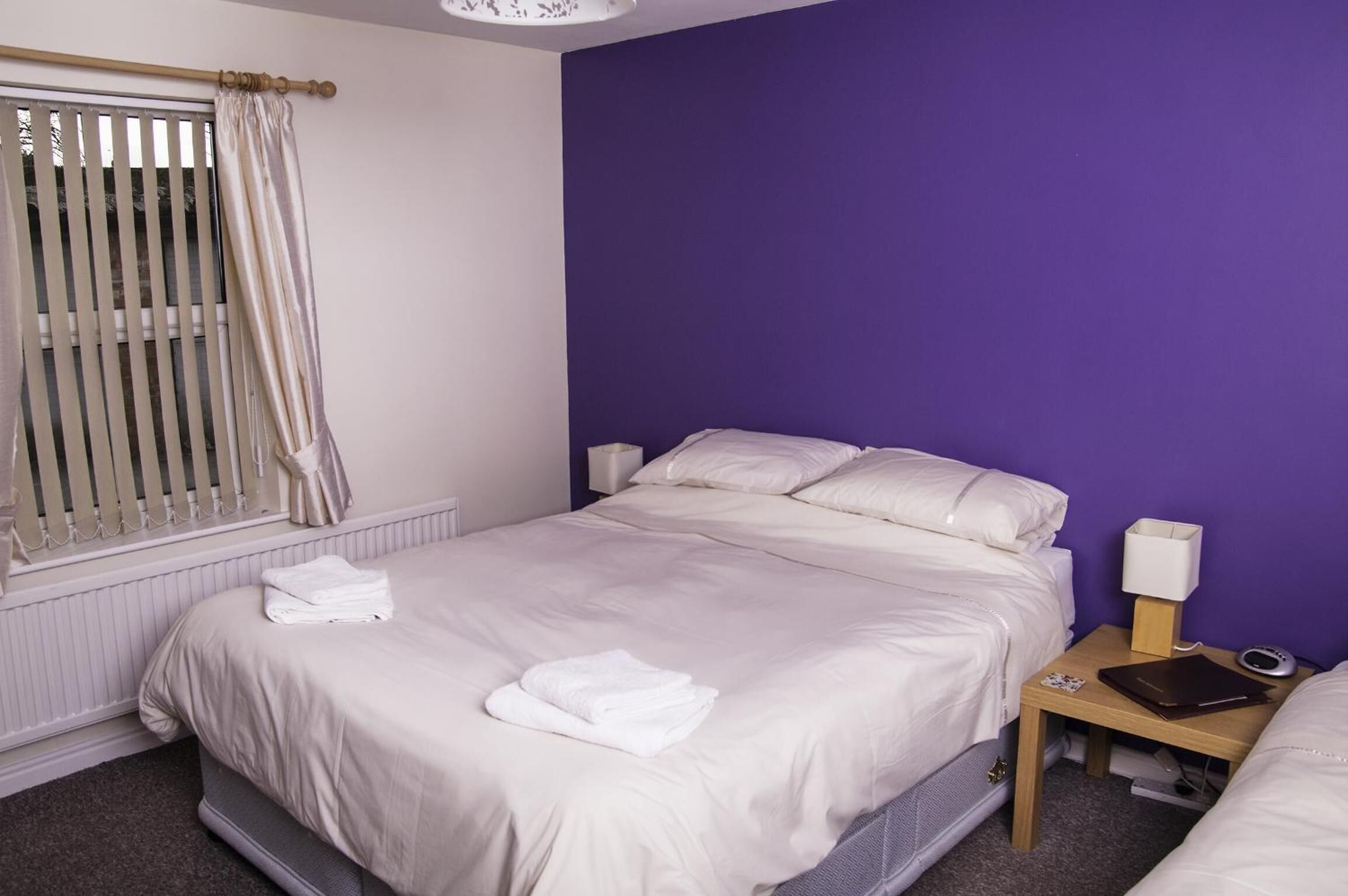 A hotel room with a bed, a nightstand, a lamp, and a window with blinds.