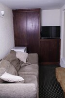 A hotel room with a bed, a TV on a stand, a wardrobe, and a patterned carpet.