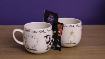 Two white mugs with cartoon animal designs and text, placed on a wooden surface against a purple background.