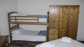 Uma cama beliche com cabeceira de madeira, um guarda-roupa de madeira com várias portas e um tapete estampado.