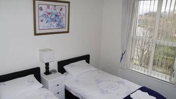 A bedroom with two single beds, a bedside table with a lamp, a framed picture on the wall, and a window with curtains.