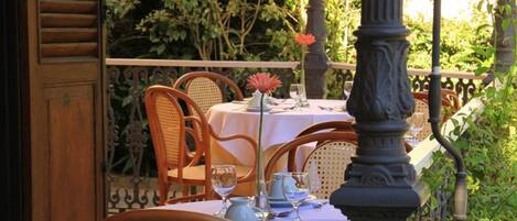 An outdoor dining area with a table set for two, surrounded by wicker chairs.