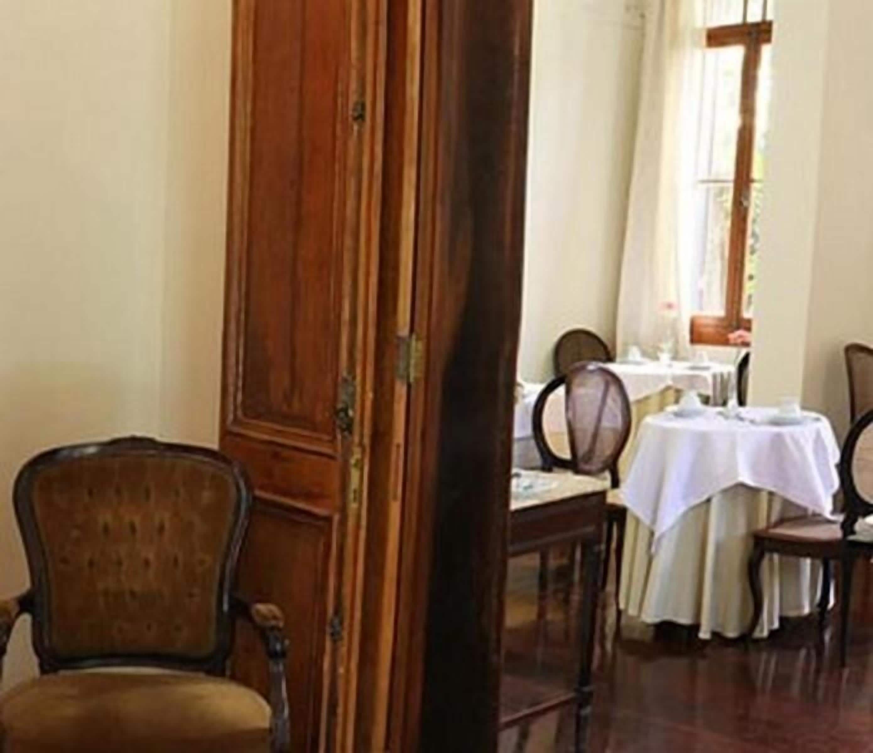 Un comedor con sillas y mesas de madera, una puerta de madera y un ventanal con cortinas.