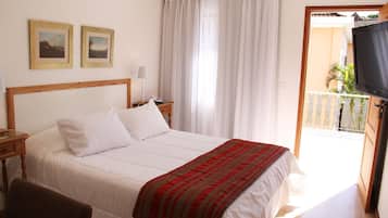 A hotel room with a bed, a nightstand, a lamp, two framed pictures on the wall, and a balcony with a TV.
