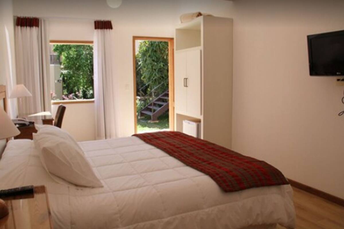A bedroom with a bed, a TV, a desk, and a window with curtains.