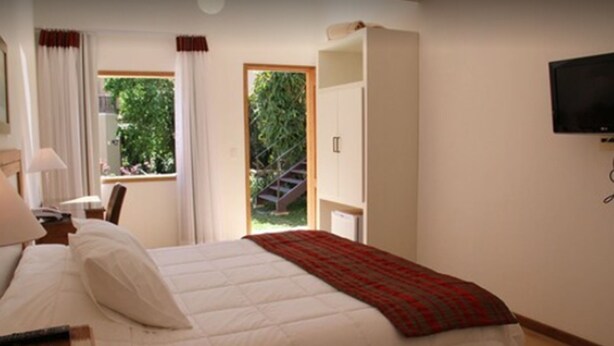 Een slaapkamer met een bed, een bureau, een stoel, een televisie en een raam met gordijnen.